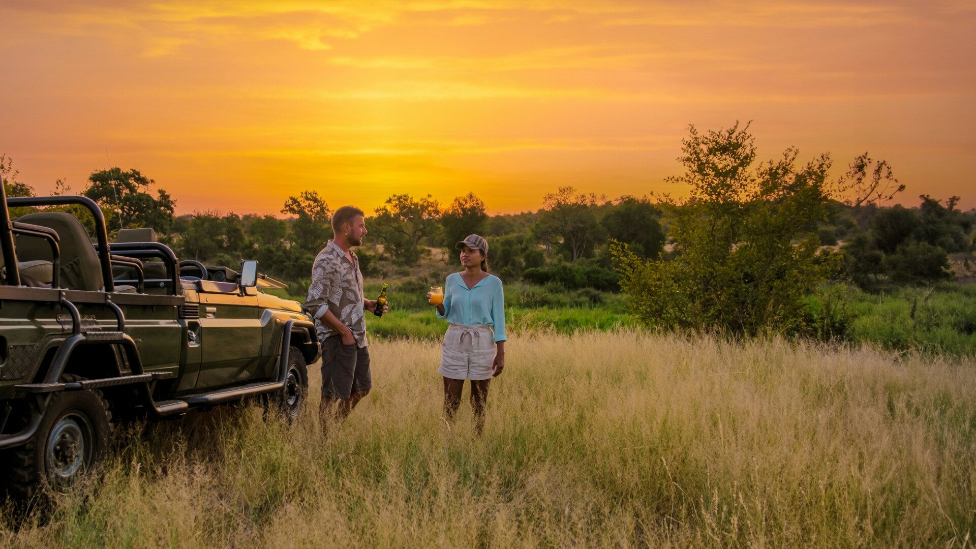 Aziatische vrouwen en Europese mannen op safari game drive in Zuid-Afrika Kruger National Park. Een paar mannen en vrouwen op safari kijken naar de zonsondergang. Toeristen op zoek sundowner met drankjes op safari